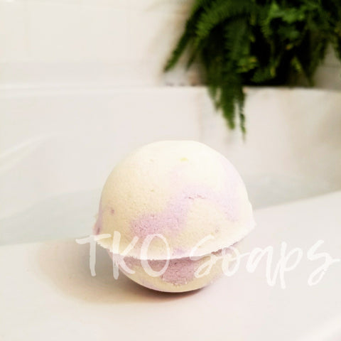 yellow and purple bath bomb on the edge of a bathtub with fern in background